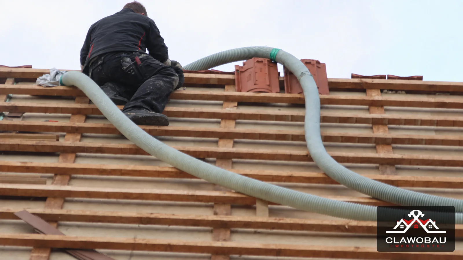Inszeniertes Symbolbild: Monteur bei einer Einblasdämmung an einer vorbereiteten Dachkonstruktion, mit Clawobau-Signatur unten rechts